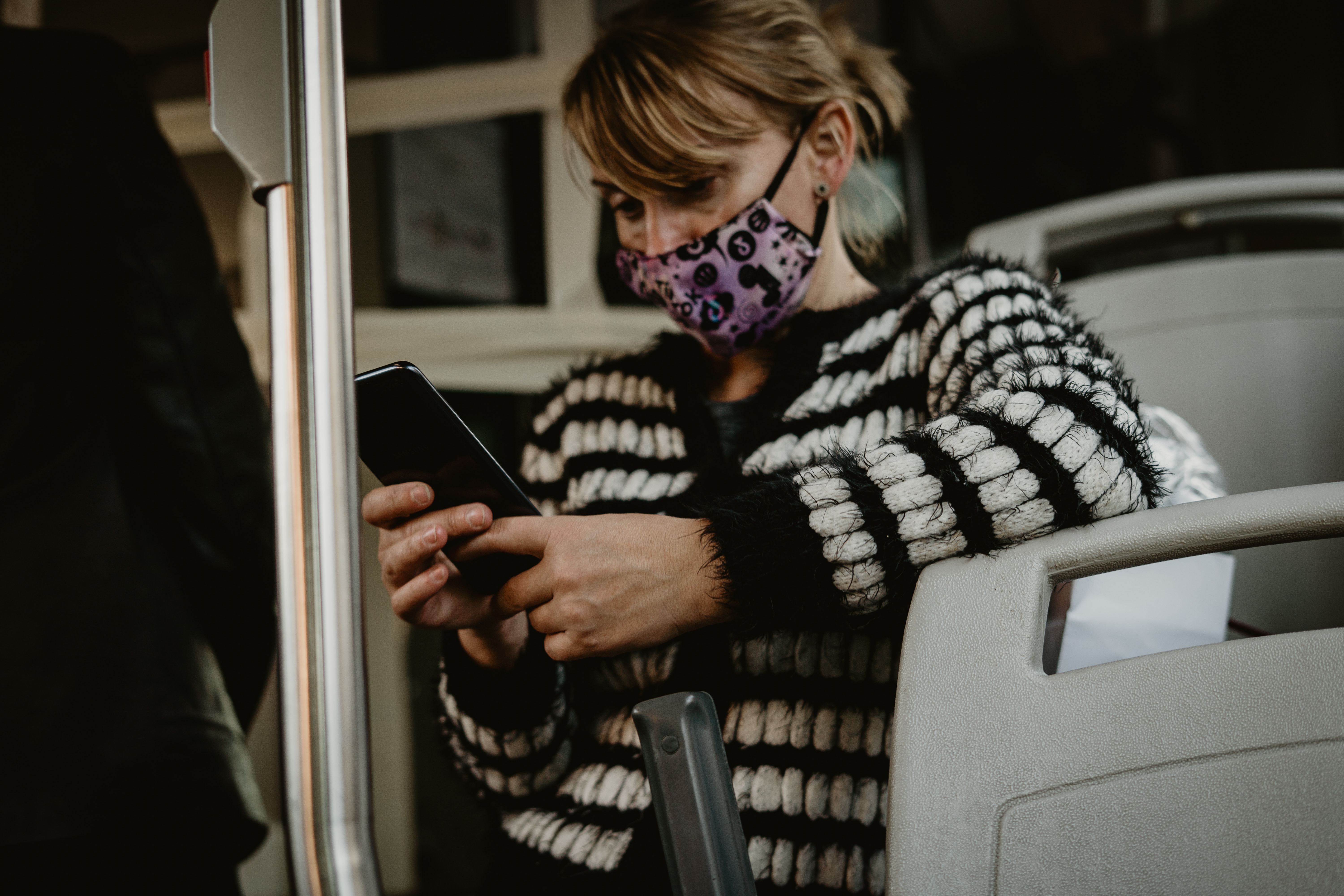 A woman in a face mask checks her mobile phone on a bus in Rome, Italy