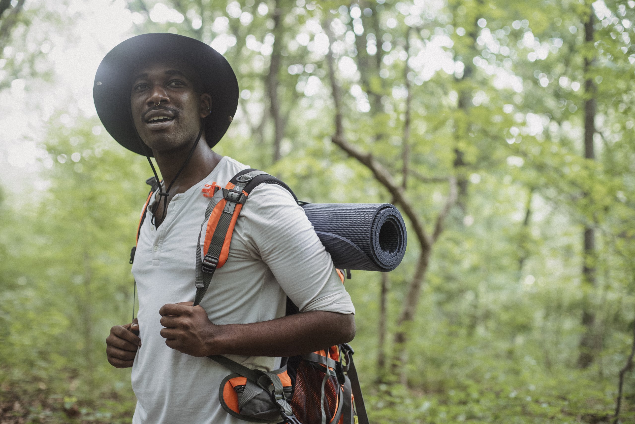 Positive black man standing with trekking backpack in forest