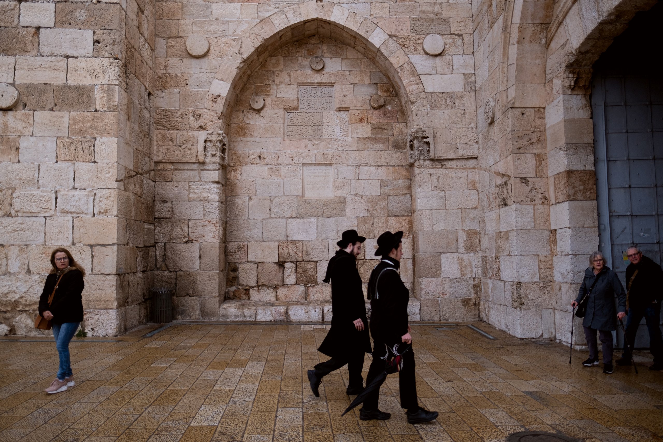 Haredim walk toward the Jaffa Gate into the Old City of Jerusalem, past a set of ancient Ottoman inscriptions.